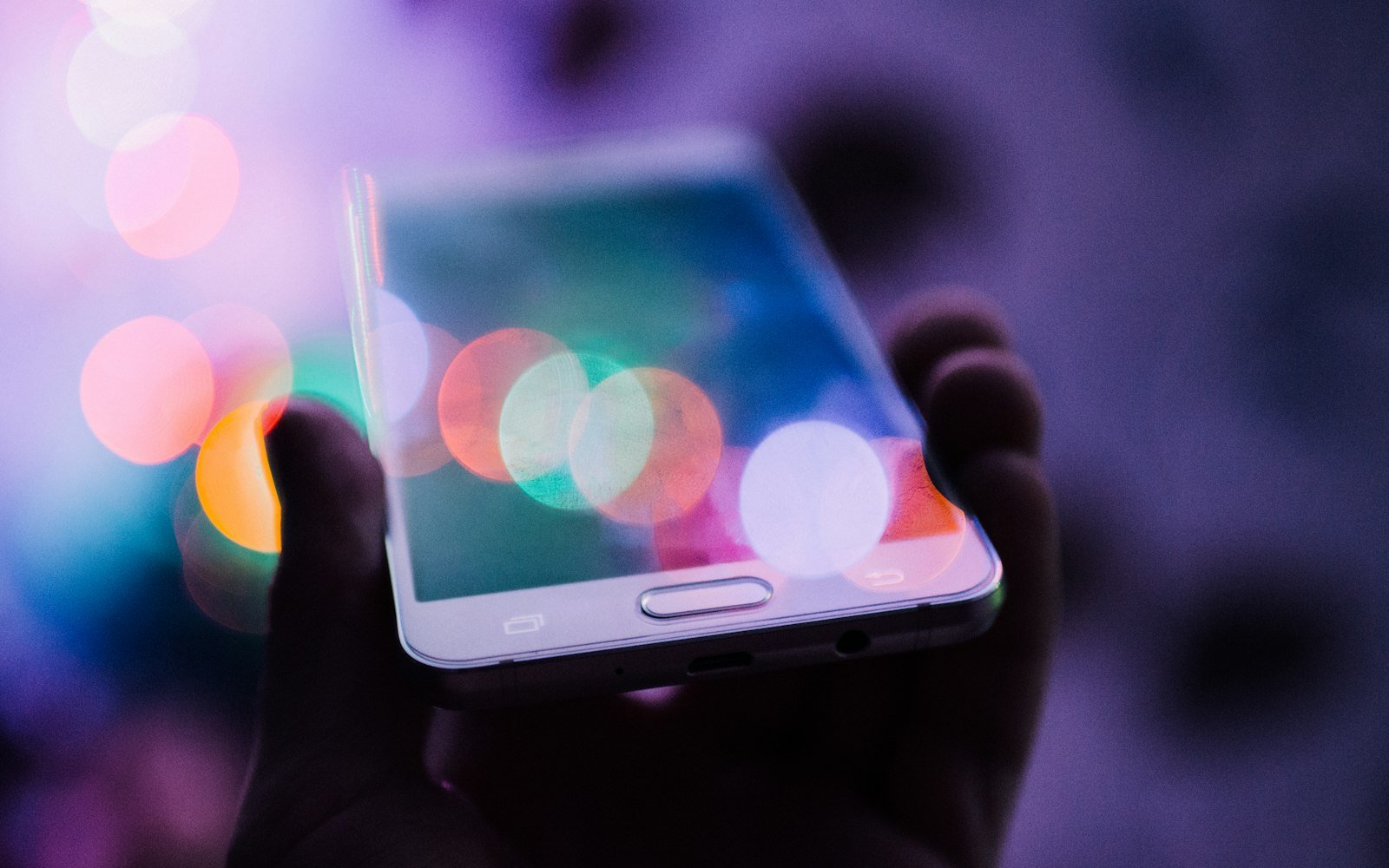 Hand holding a smartphone with coloured lights behind