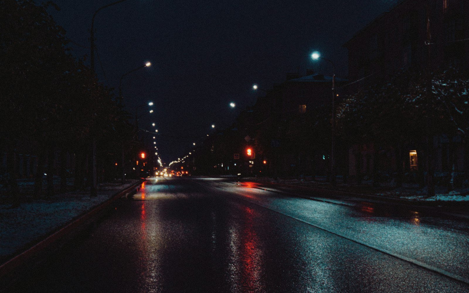 Wet city road at night with traffic lights in the distance