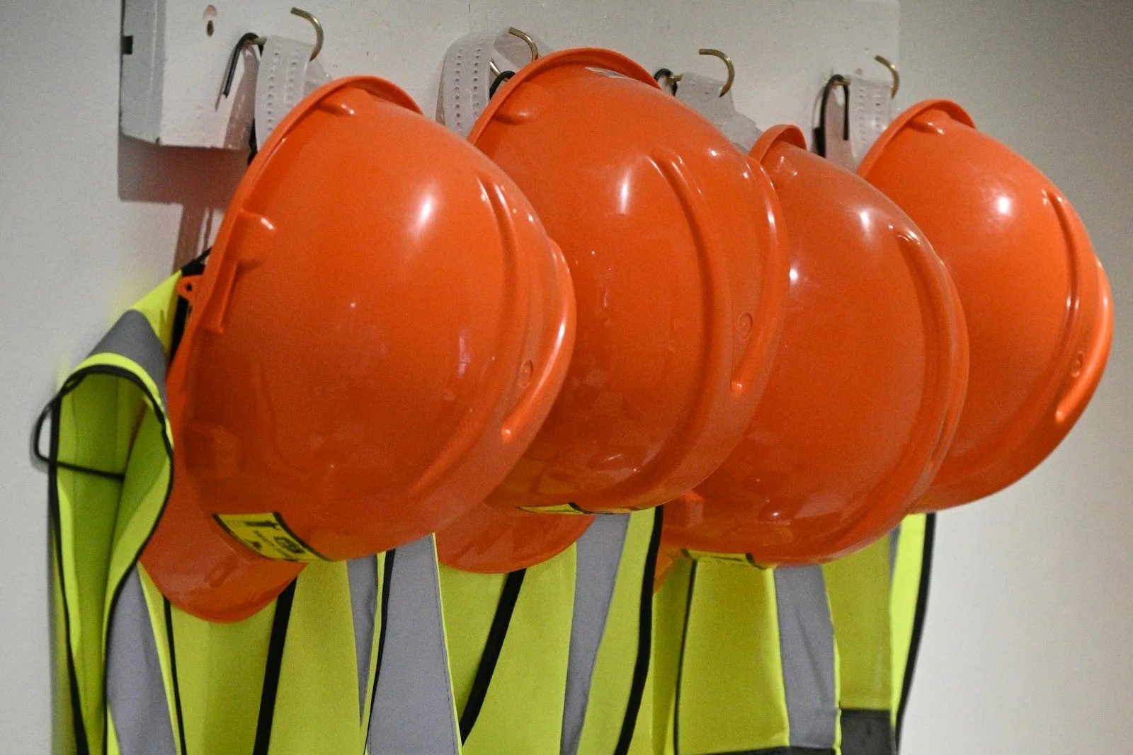 Orange hard hats and high-visibility safety vests hanging on a wall