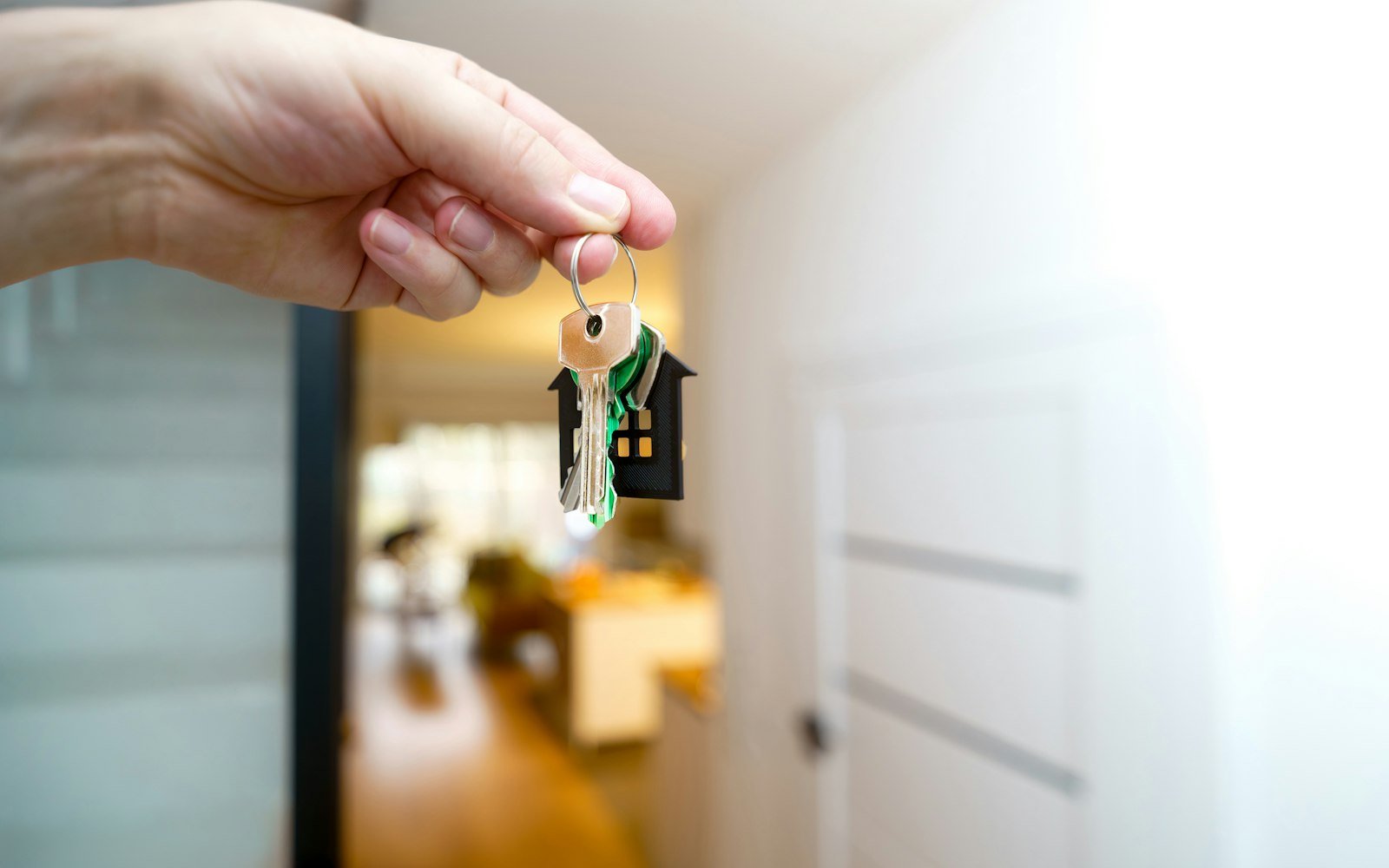 A hand holding house keys in front of an entrance