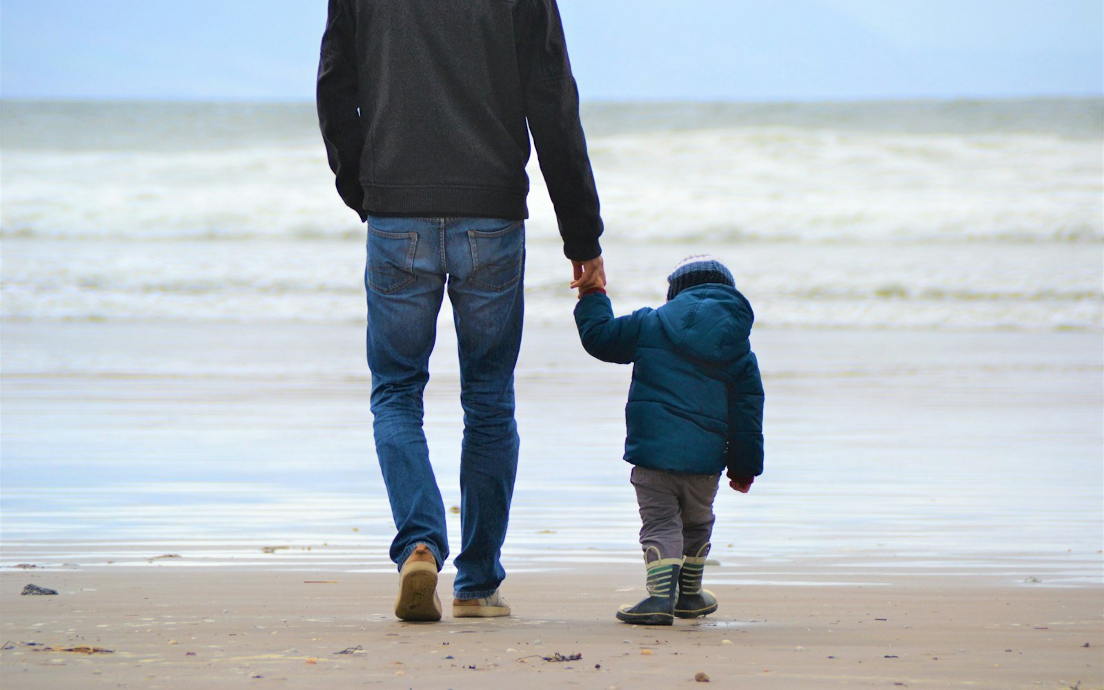 A parent and child holding hands at the edge of the water
