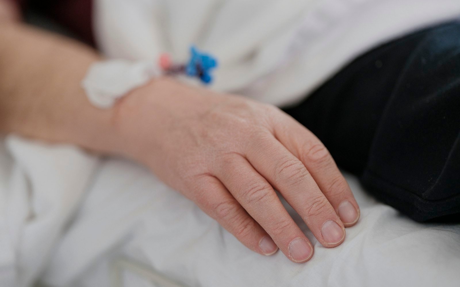Hand resting on a hospital bed sheet