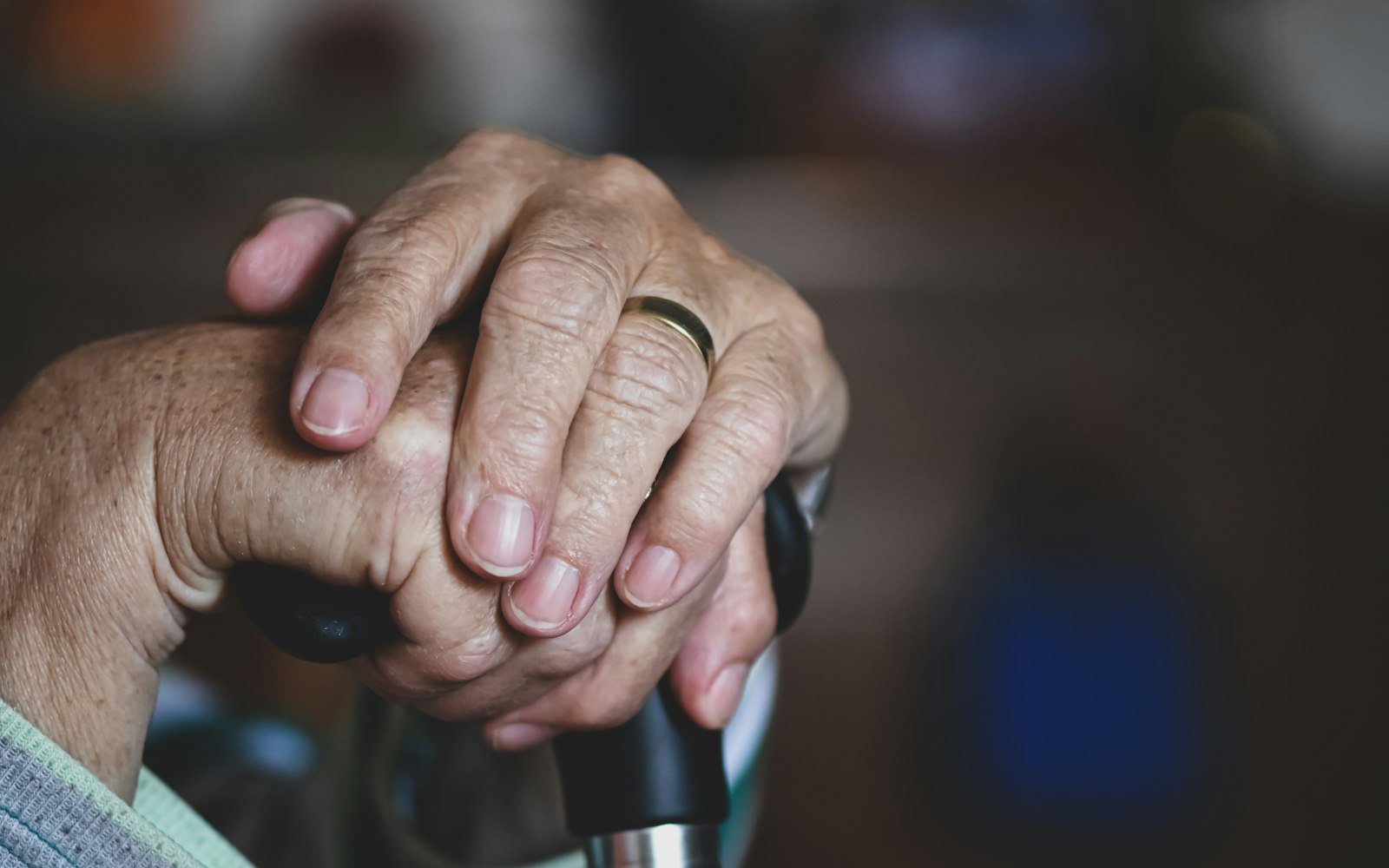 Older hands with a gold ring resting on a cane